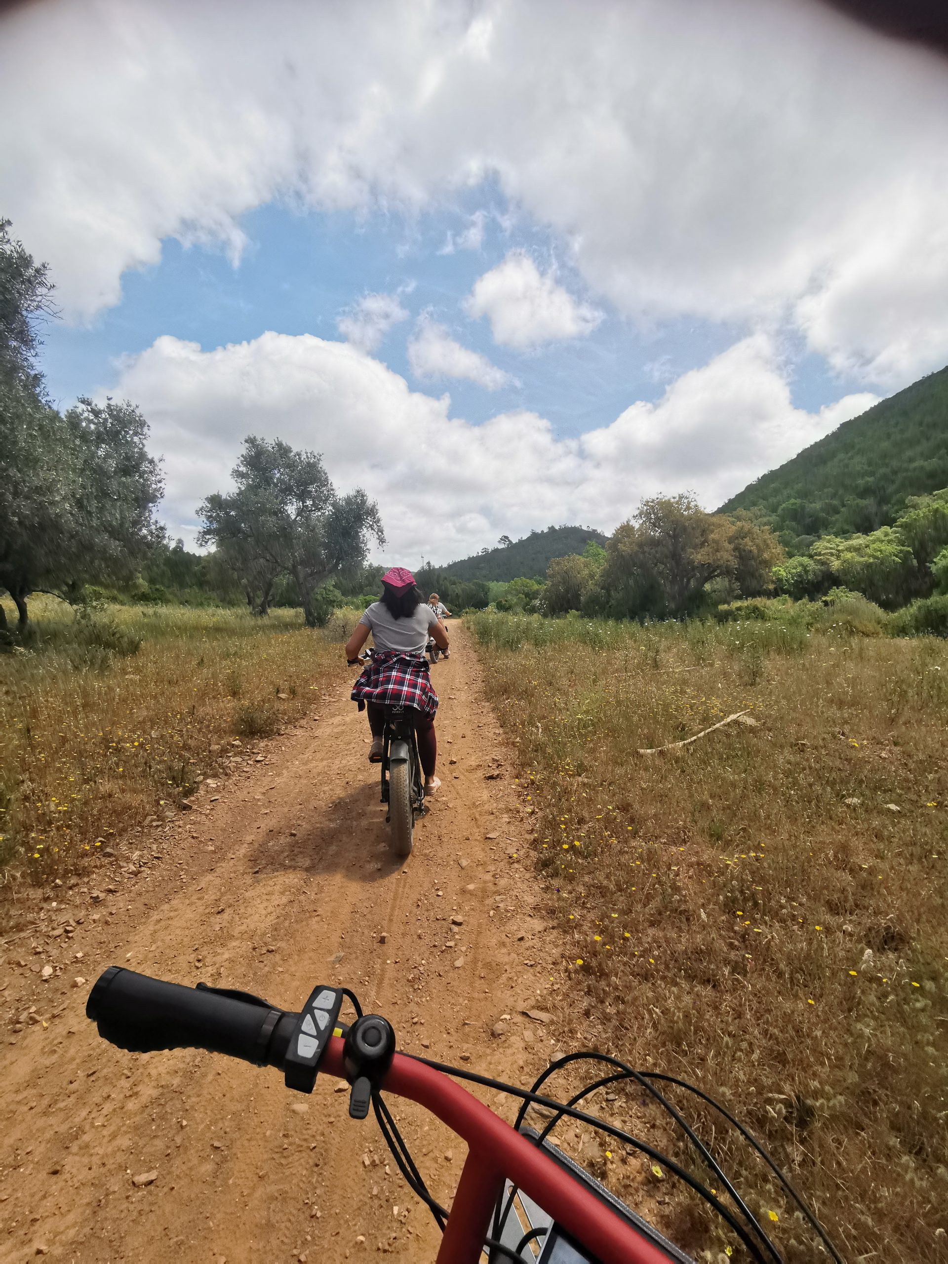 Pamela cycling away on the fat tyre ebike on a sandy road towards Bordeira